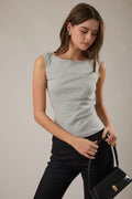 Woman wearing a sleeveless polka dot top and holding a black handbag against a neutral background
