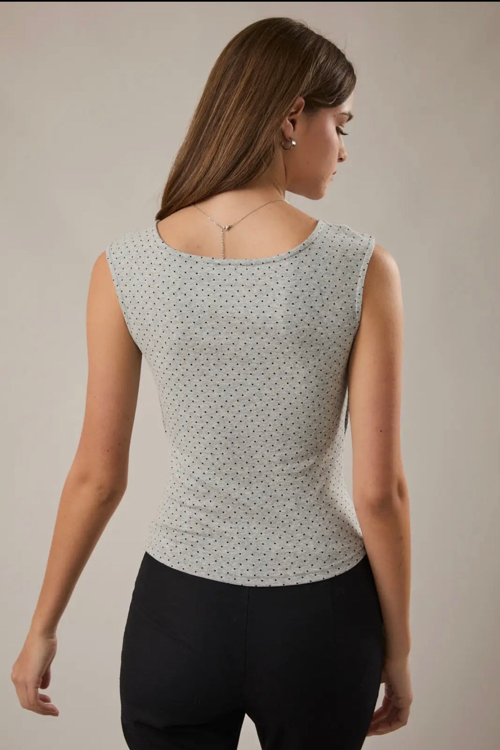 Woman wearing a sleeveless top with a subtle pattern on a plain background