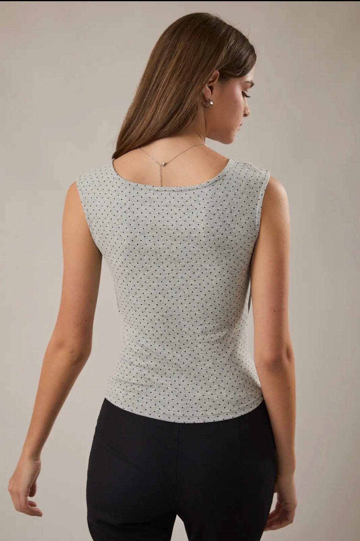 Woman wearing a sleeveless top with a subtle pattern on a plain background