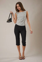 Woman wearing a sleeveless top and black pants holding a small black handbag against a neutral background