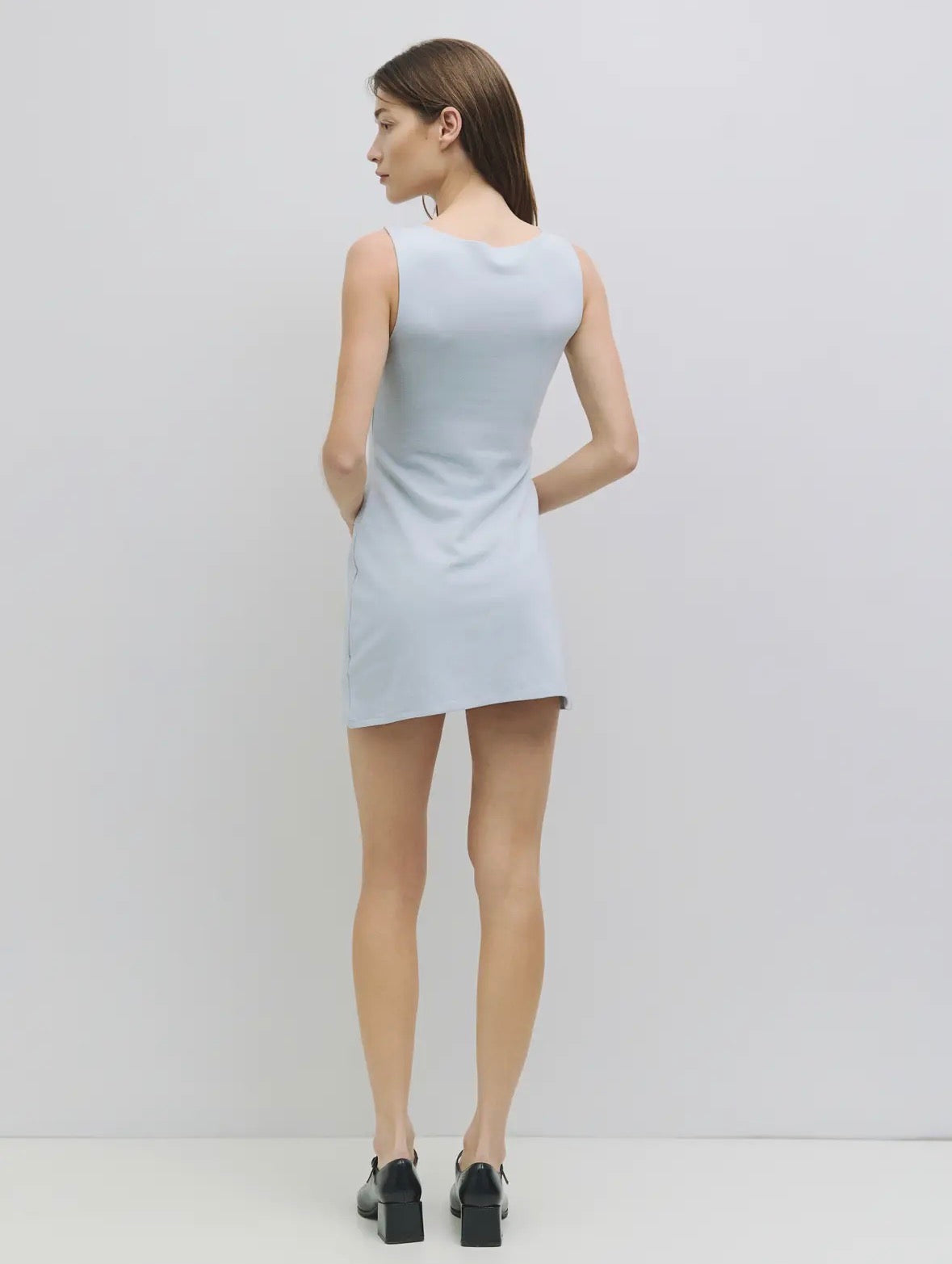 Woman wearing a light blue sleeveless dress on a plain background