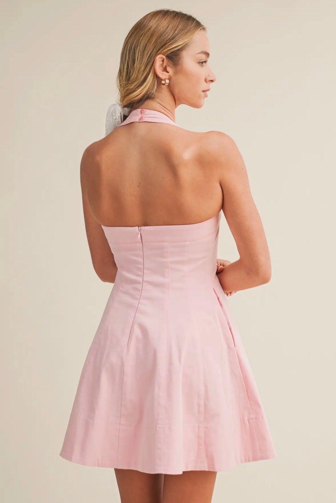 Woman wearing a pink halter neck dress against a beige background