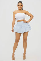 Woman wearing a white strapless top and light blue pleated skirt on a plain background