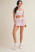 Woman wearing a white sports bra and pink skirt on a beige background