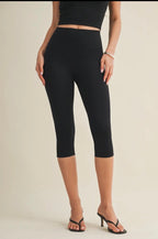 Person wearing black capri leggings on a plain background