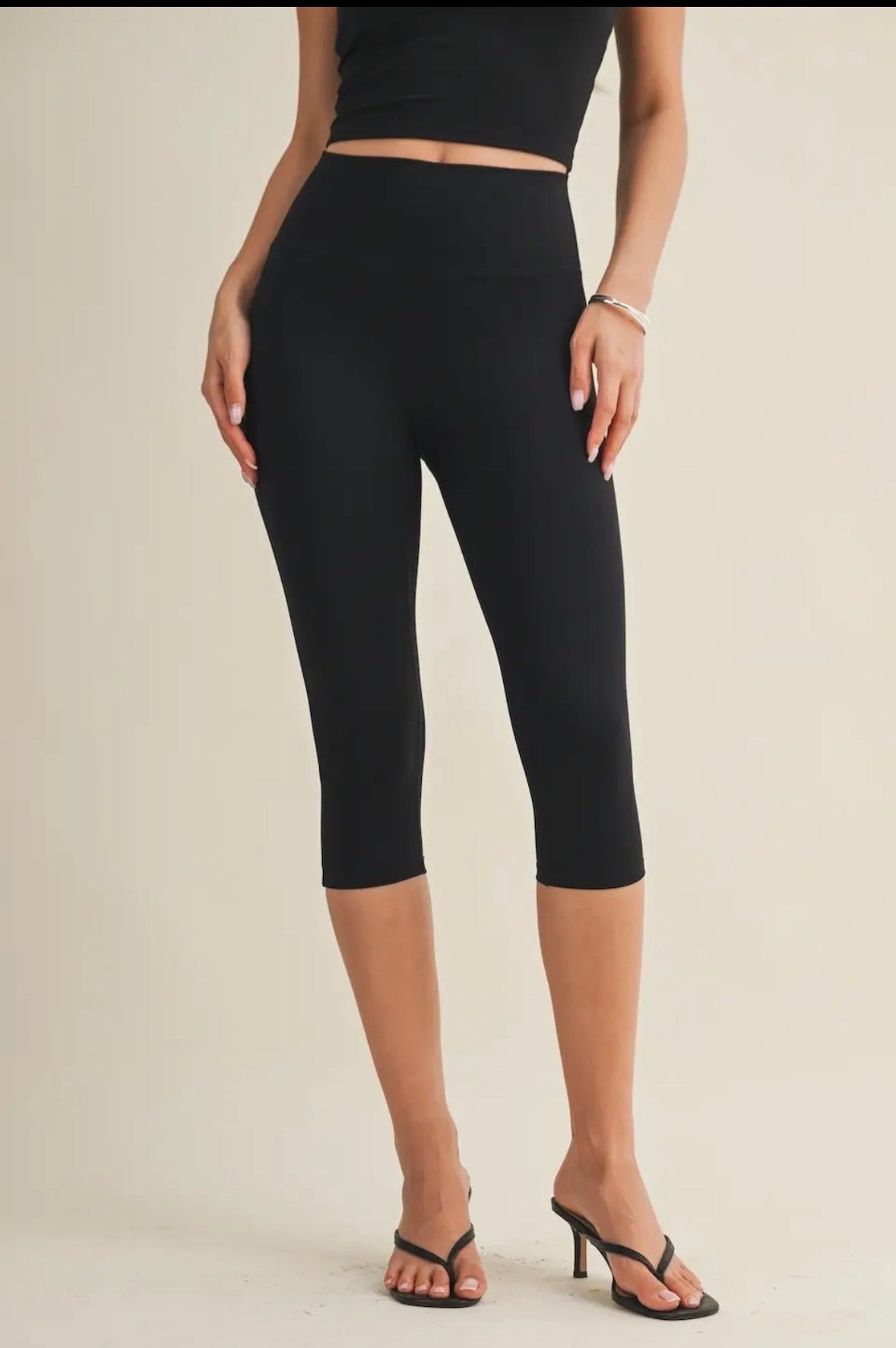 Person wearing black capri leggings on a plain background