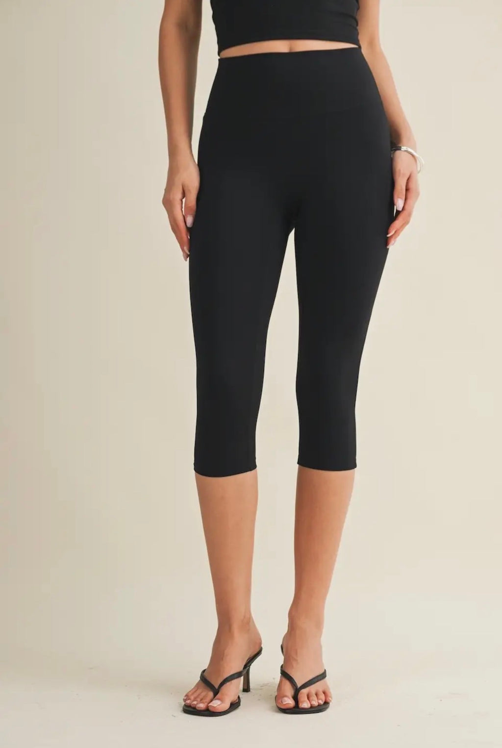 Person wearing black capri leggings on a beige background