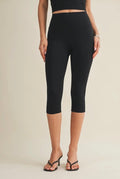 Person wearing black capri leggings on a beige background