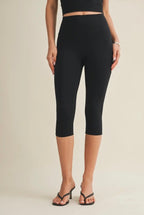 Person wearing black capri leggings on a beige background