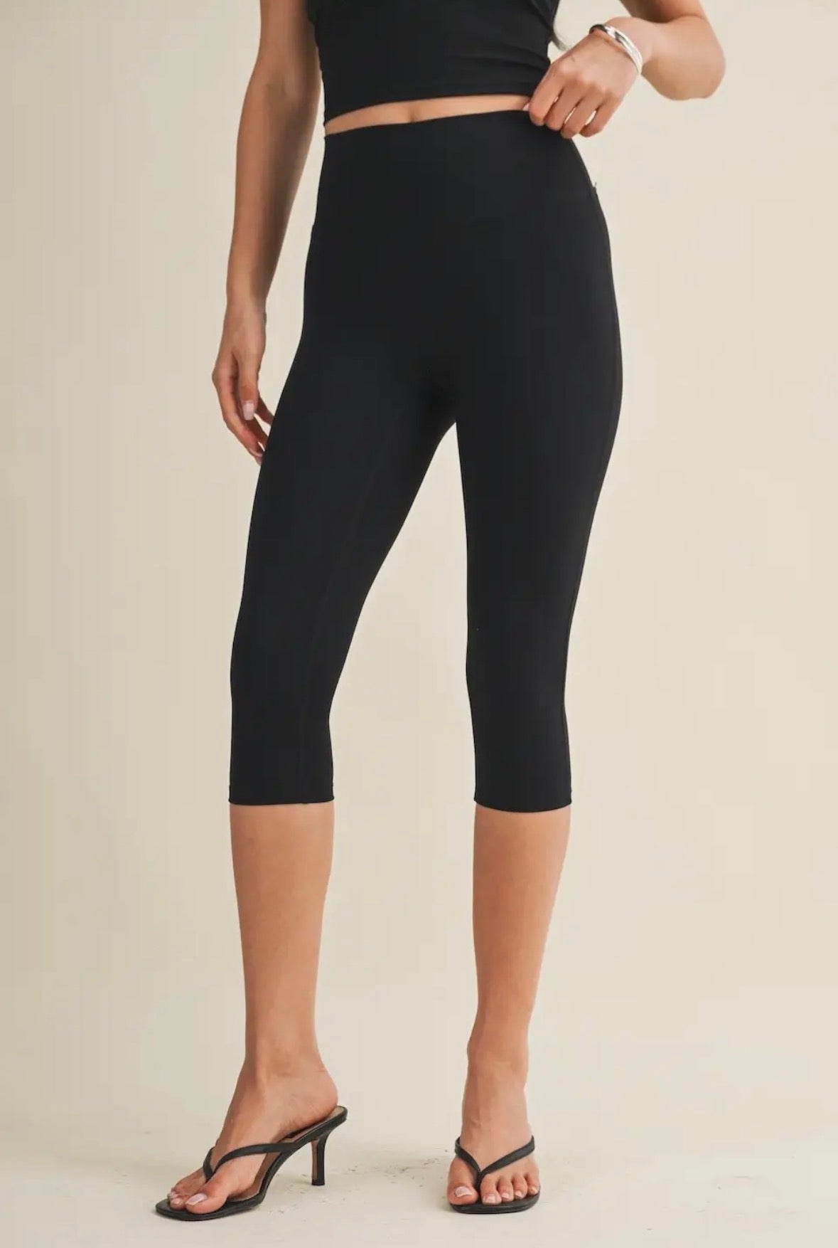 Person wearing black capri leggings on a beige background