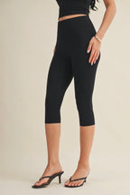 Person wearing black capri leggings on a beige background