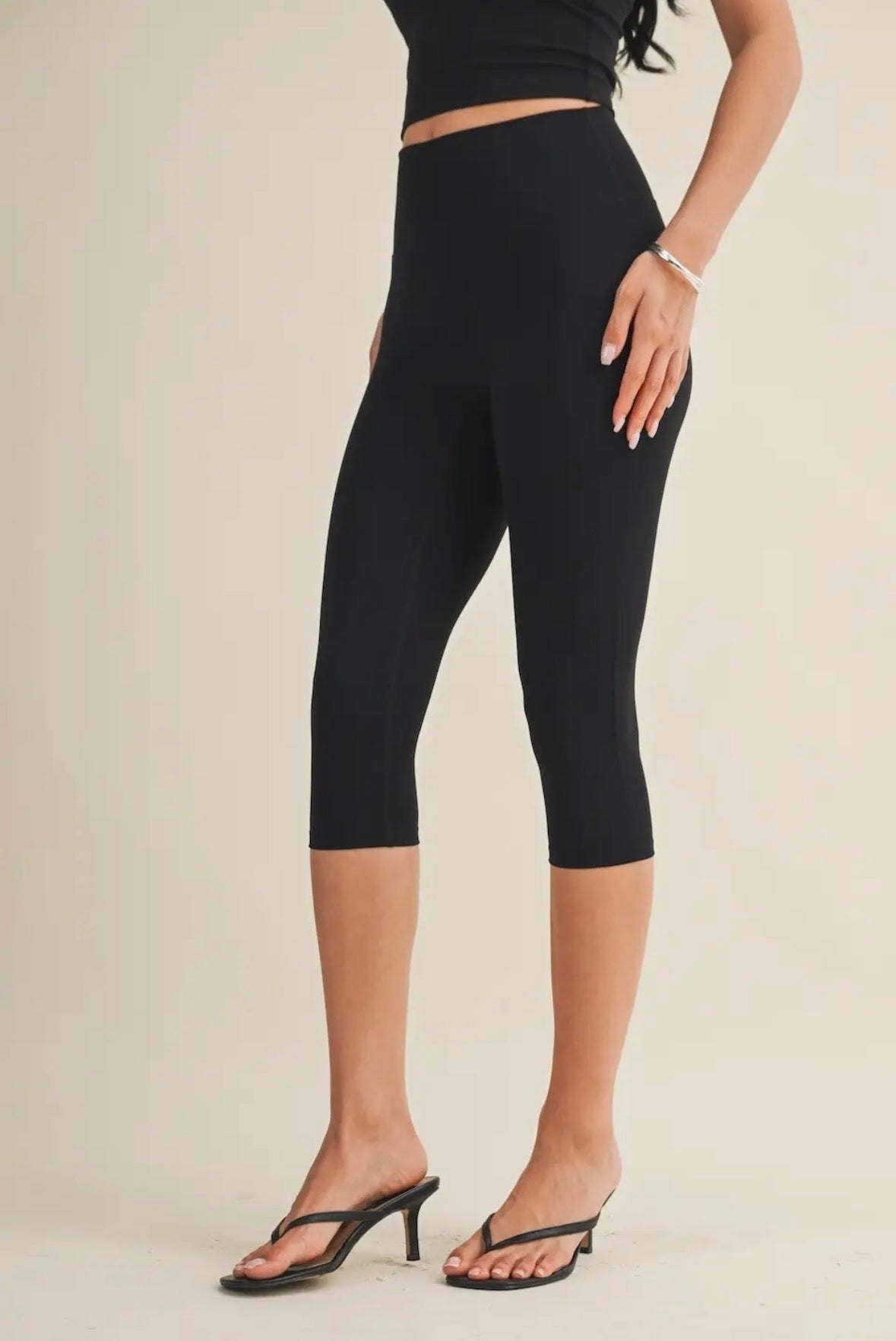 Person wearing black capri leggings on a beige background