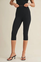 Person wearing black capri leggings on a beige background