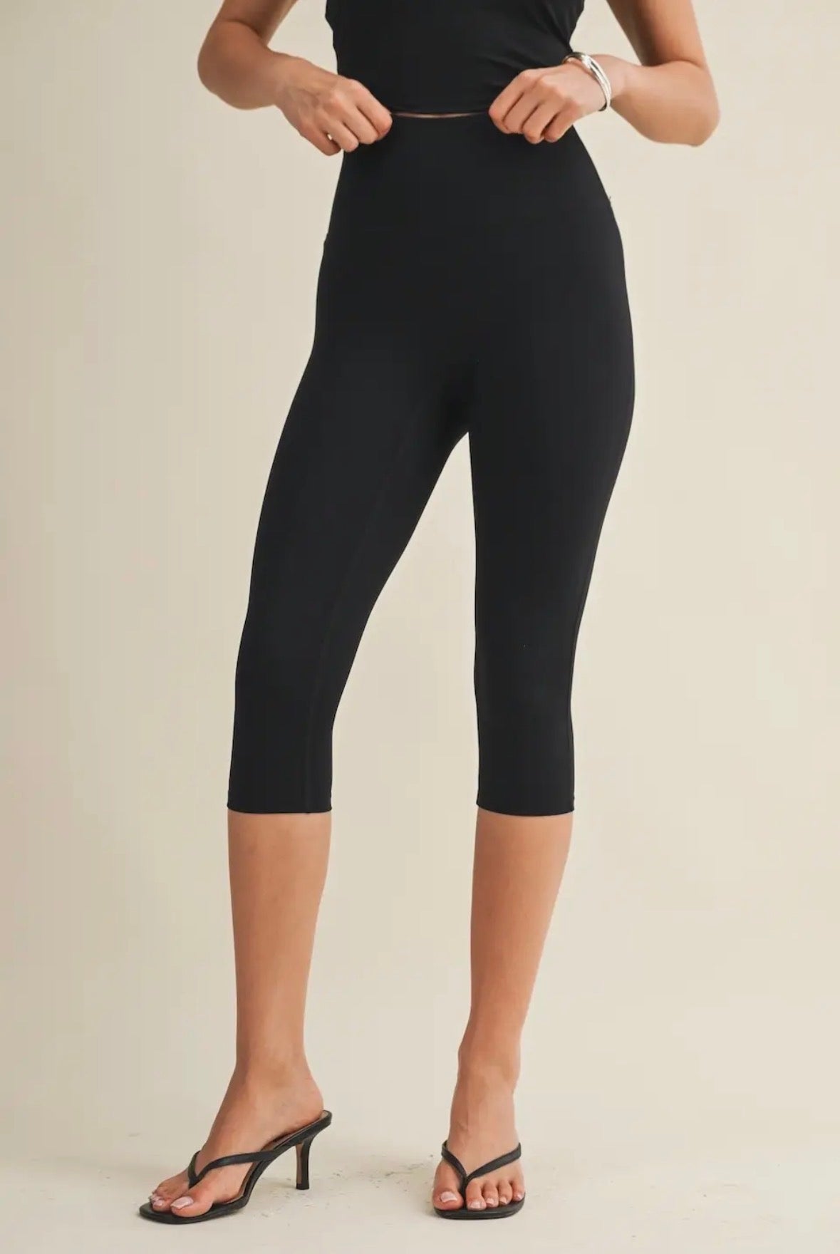 Person wearing black capri leggings on a beige background