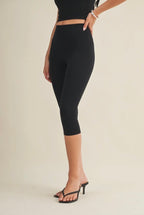 Person wearing black capri leggings on a beige background