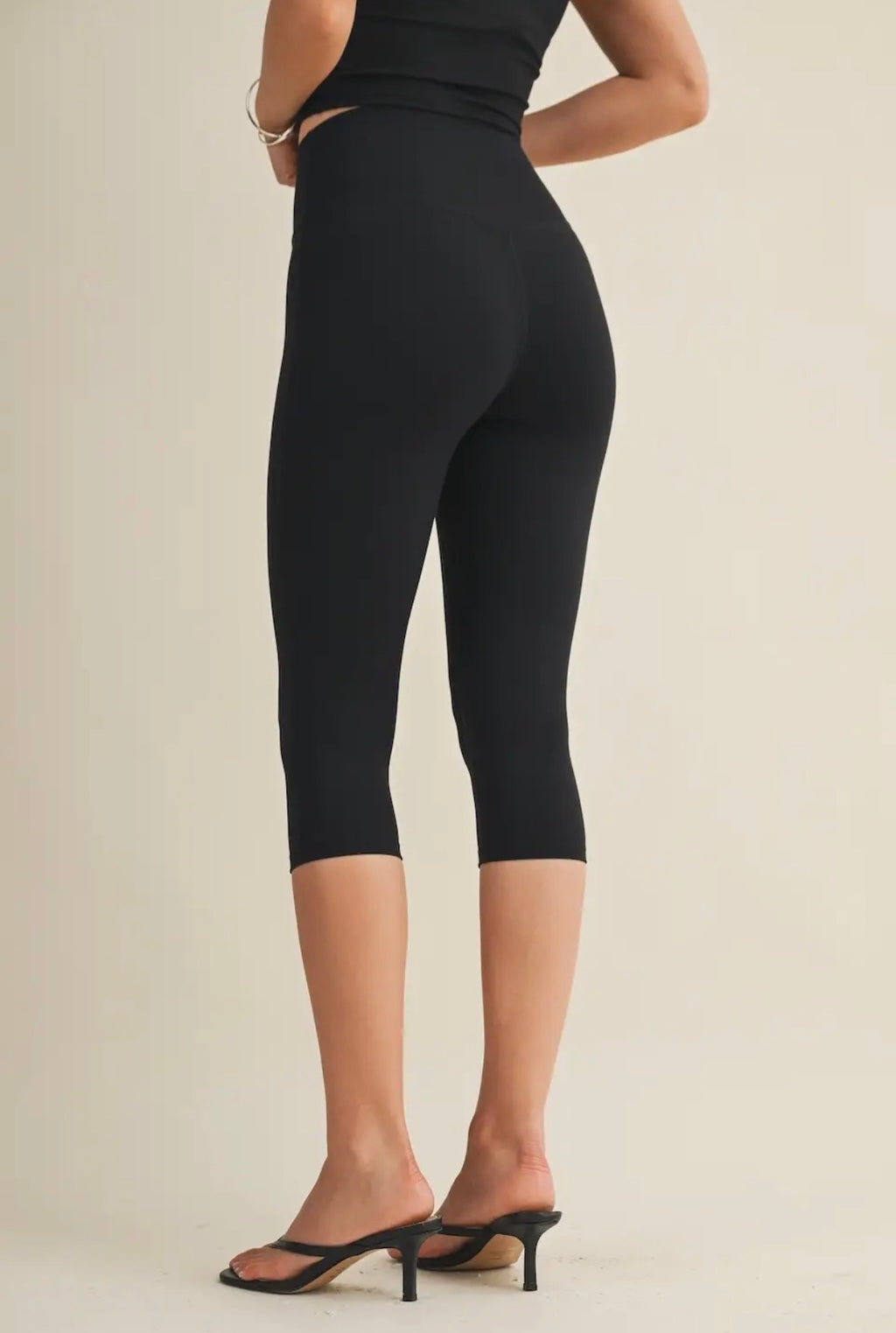 Person wearing black capri leggings on a beige background