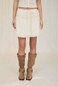 Person wearing a white skirt and brown boots on a plain background