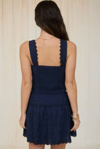 Navy blue dress with scalloped edges worn by a person on a plain background
