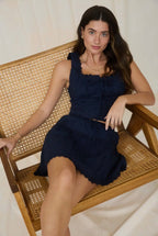 Woman in a navy dress sitting on a wicker chair against a white background