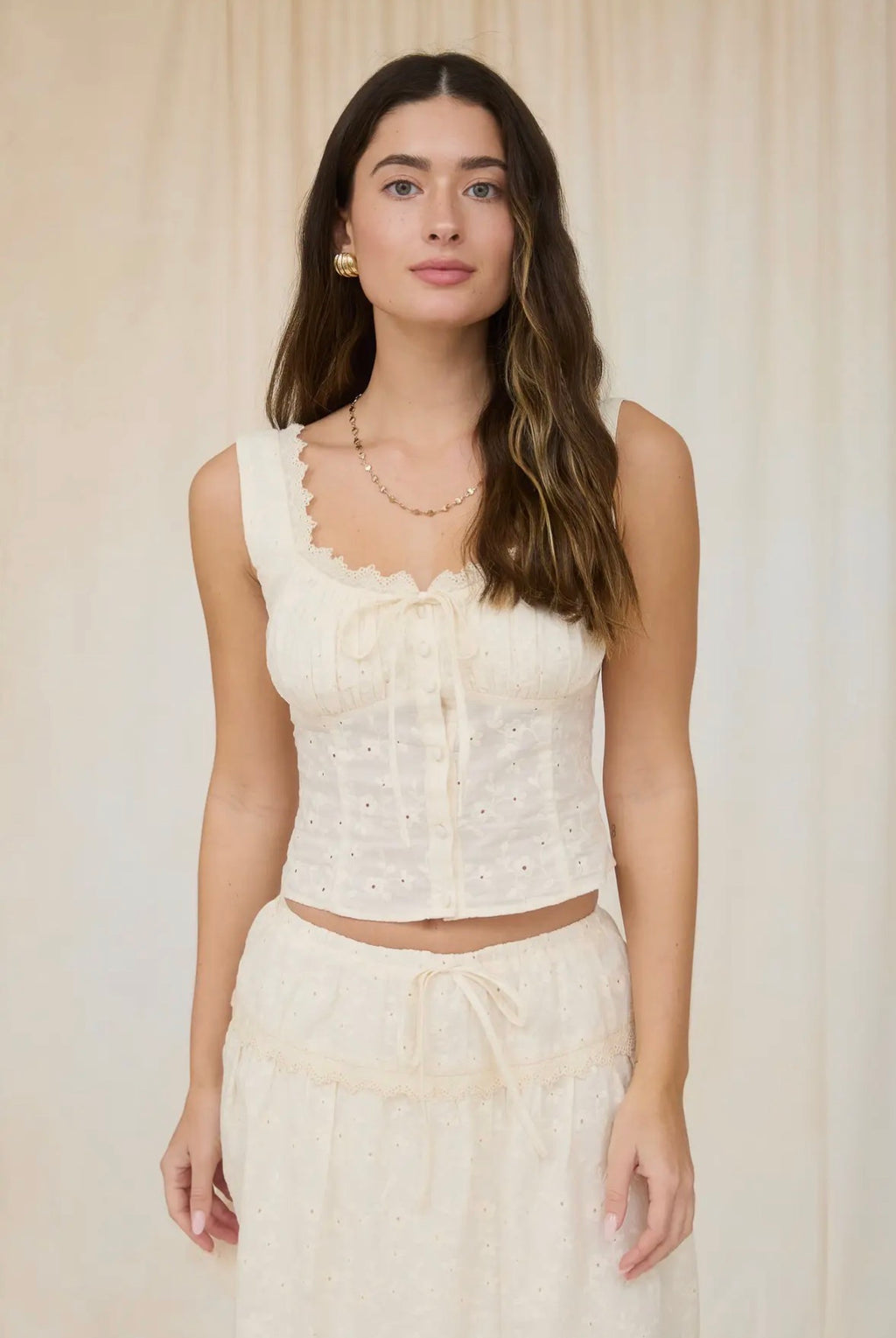 Woman wearing a white lace top and skirt against a plain background