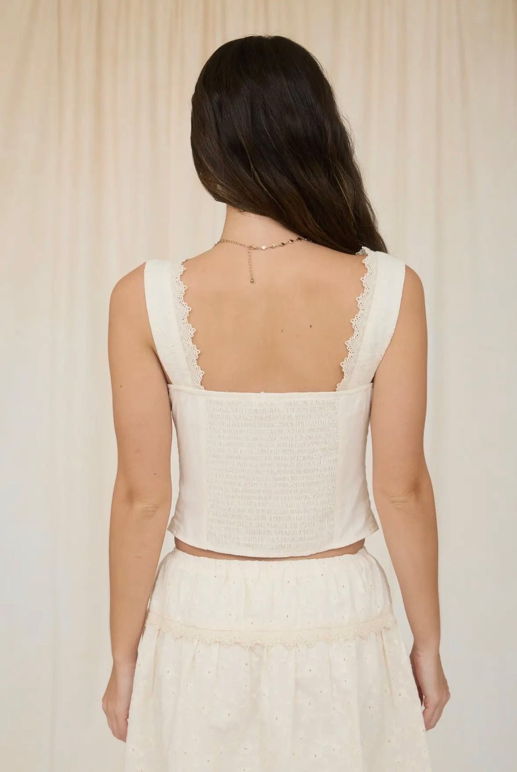 Woman wearing a white sleeveless top with a sheer back panel against a neutral background