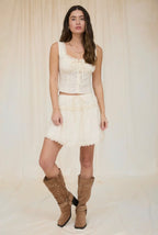 Woman wearing a white dress and brown boots against a plain background